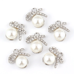 Detail of silver alloy bow pendants with rhinestones and white pearls for DIY jewelry