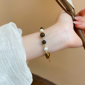 Elegant gold-plated bracelet with pearls and tiger eye stones worn by a model