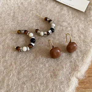 Tiger eye C-shaped hoop earrings and brown resin drop earrings on warm plush background