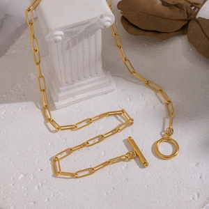 Minimalist gold paperclip chain necklace with OT toggle clasp on a textured white surface