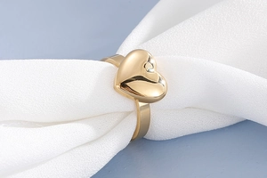 Gros plan d'une bague coeur dorée polie présentée sur un tissu de soie blanche