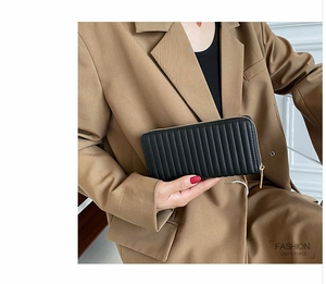 Detail showing hand holding a black quilted PU leather long wallet with golden zipper