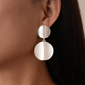 Close-up of geometric silver double disc earrings with a brushed metallic texture