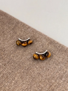 Detail of silver drop earrings with three tiger eye stones on brown knit background