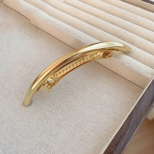 Macro detail of a minimalist gold curved metal hair clip on a beige textured display tray