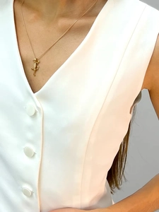 Close-up of a stylish gold gecko lizard pendant necklace worn over a white V-neck vest