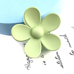 Detail view of large matte flower hair claw clip in light green on decorative backdrop