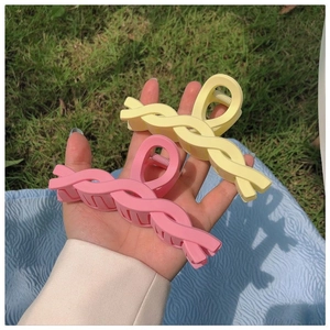 Detail showing yellow and pink twist-shaped hair claws held against a grass background