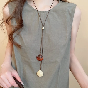 Close-up of shell pendant necklace on olive green linen clothing with a natural aesthetic