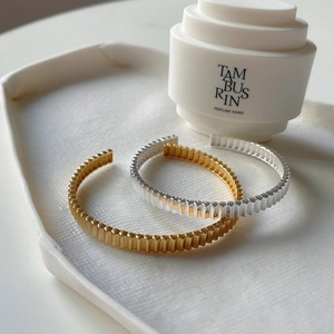 Irregular textured open bangles in gold and silver finish on a ceramic tray