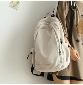 Close-up of minimalist cream nylon backpack showing spacious compartments and zippers