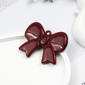 Macro detail of dark red glossy acrylic bow charm with hanging ring for DIY jewelry making