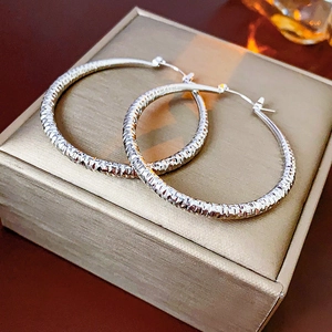 Gros plan de boucles d'oreilles créoles texturées argentées sur un écrin à bijoux beige