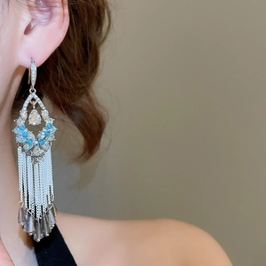 Close-up of sparkling floral silver tassel earrings with blue crystals on model