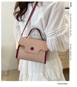Detail of a two-tone textured leather crossbody bag with a red round buckle