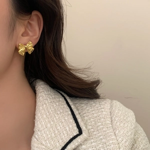 Elegant gold bow earrings with polished finish shown worn on ear for stylish fashion
