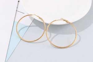 Detailed view of large gold twisted rope hoop earrings resting on a white ceramic plate