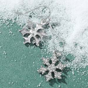 Macro shot of silver snowflake drop earrings with white rhinestones on green winter background