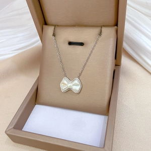 Detailed view of titanium steel necklace with an iridescent pearl bow pendant in a beige box