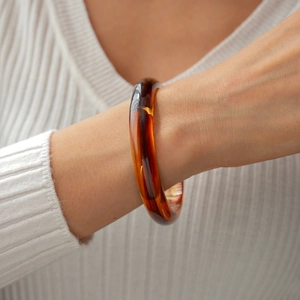 Close-up of translucent amber acrylic bangle featuring a smooth geometric circular design