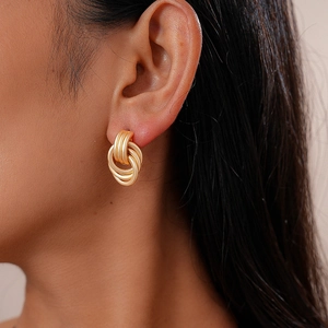 Close-up of golden multilayer geometric hoop earrings worn by a model in soft lighting