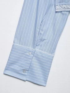 Détail du poignet d'une chemise à rayures avec dentelle blanche et deux boutons transparents