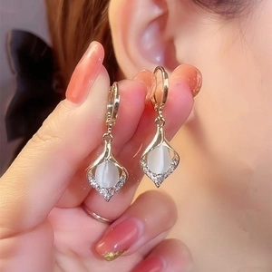 Elegant gold teardrop earrings with white cat eye stone and crystal accents on model