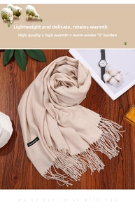 Detail view of light beige cashmere scarf with tassels and black fabric tag on wood
