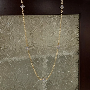 Close-up of golden necklace featuring five light blue clover charms on a vintage chain