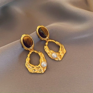 Detail of vintage gold earrings with tiger eye stone and small white pearl on grey fabric