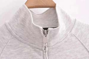 Detail view of a gray cotton stand collar sweatshirt with a metallic zipper closure