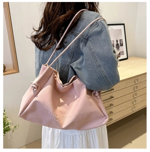 Detailed side view of large soft pink leather tote bag with embossed letters on a model