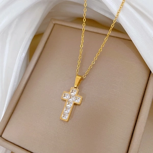 Detailed view of a gold cross necklace with square zircons on a beige jewelry cushion