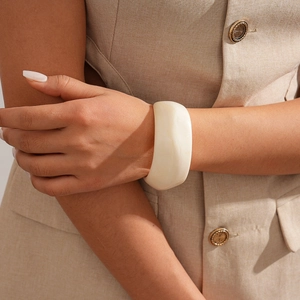 Detail of wide cream resin cuff bracelet styled with a minimalist khaki blazer sleeve