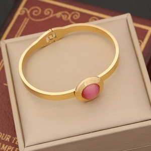 Retro gold stainless steel bangle featuring a pink oval opal stone on a vintage book