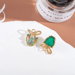 Golden apple-shaped earrings with opal and green gemstones and crystal bows on a stone base
