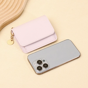 Mini portafoglio rosa in pelle con trama litchi e ciondolo d'oro vicino a cellulare