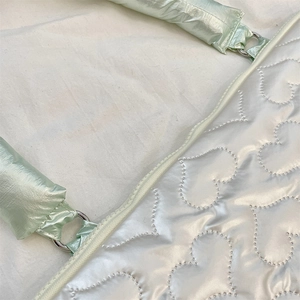 Detail of heart quilting on a glossy white tablet bag with a metallic green strap