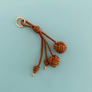 Detailed view of hand-woven brown rope bag charm with golden metal ring and knots