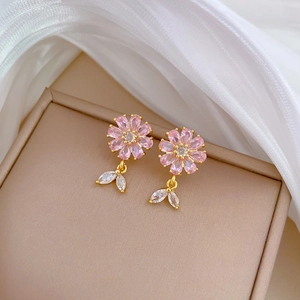 Macro shot of pink floral earrings with gold plating and white leaf charms on a jewelry box