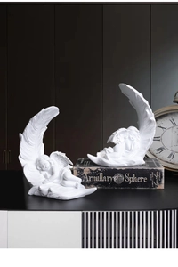 Detailed view of two white resin angel sculptures resting on large feather wings