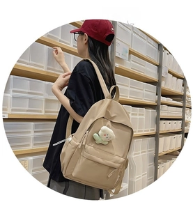 Side view of a beige nylon backpack with a plush flower charm worn by a model in a store