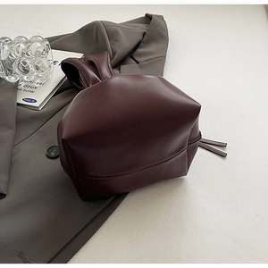 Detail of burgundy bucket bag with drawstring closure and knotted handle on gray background