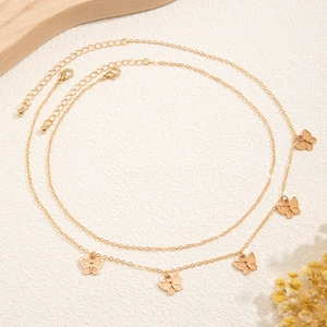 Detailed close-up of golden butterfly pendant necklaces on textured beige background