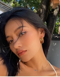 Detailed close-up of C-shaped gold earrings with amber resin inlays worn by a model