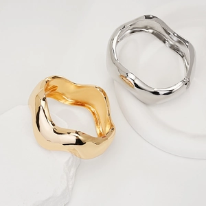 Close-up of irregular wave gold and silver cuff bracelets on textured white marble