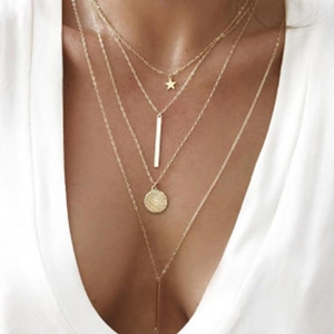Golden multi-layer necklace with star, bar, and tassel charms worn on white clothes