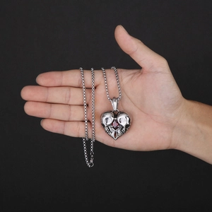 Detail of silver skull heart pendant with red gem held in hand for size scale