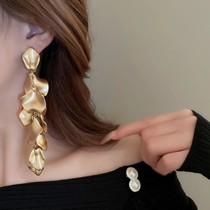 Detail of model wearing long gold layered petal tassel earrings with a matte metallic finish