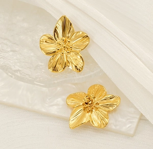 Nahaufnahme goldener Blütenohrringe mit gebürsteter Metallstruktur und Blumendesign